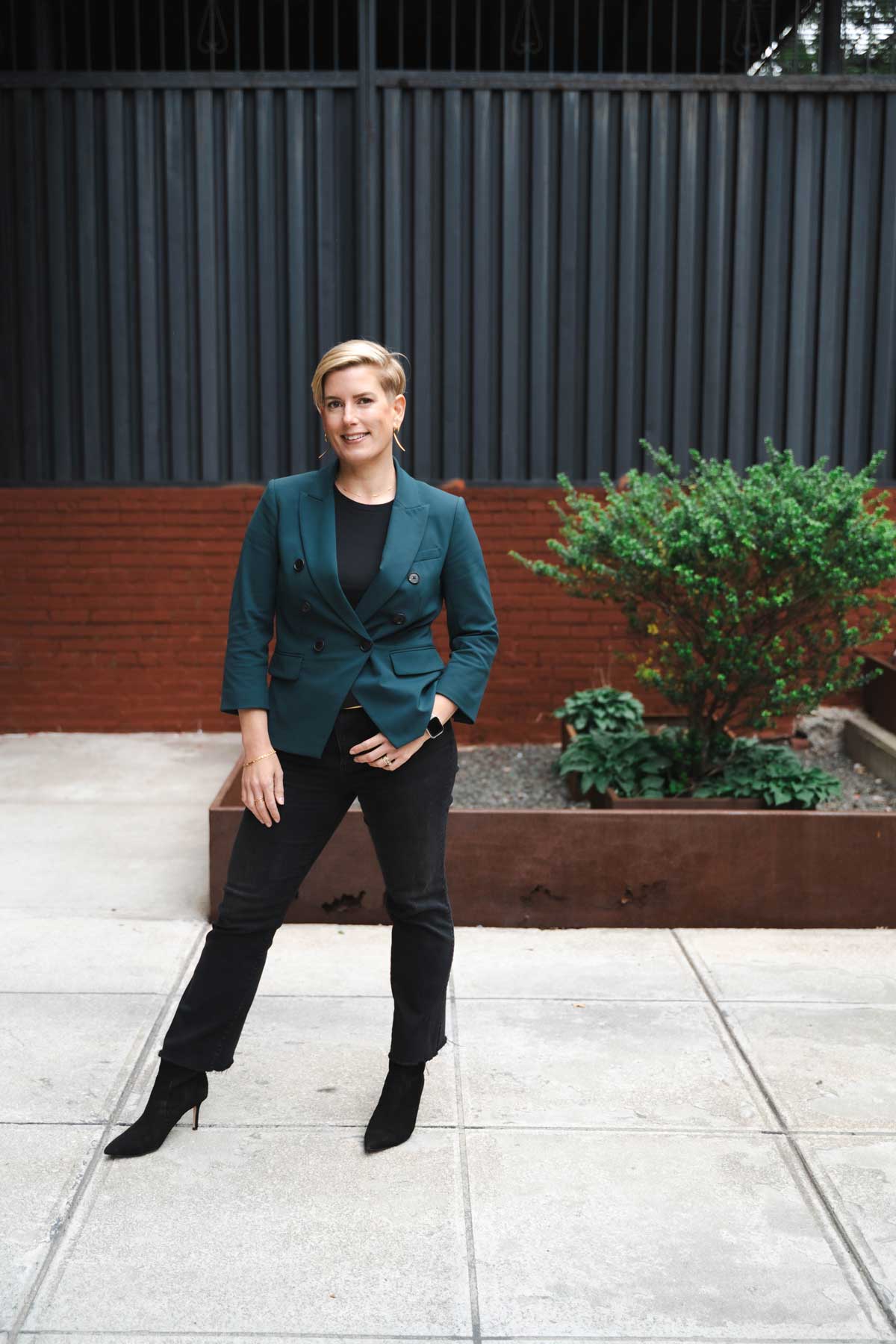 Janel Simms standing with teal blazer, black jeans, and black heels.